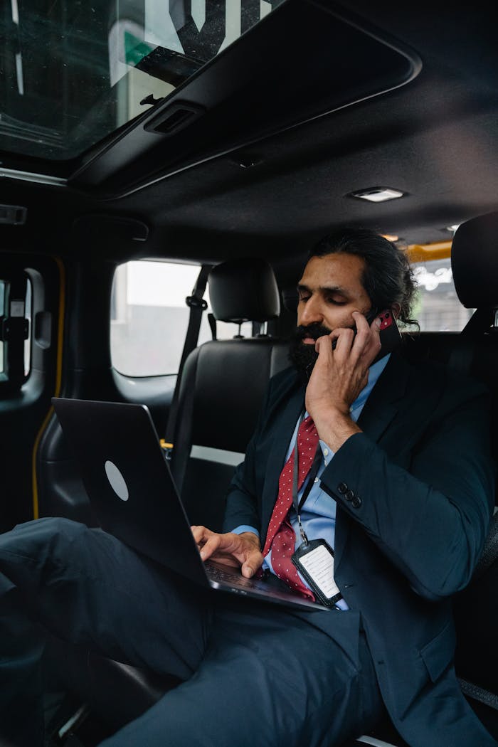 Professional man in a suit working on laptop and phone in back of taxi.