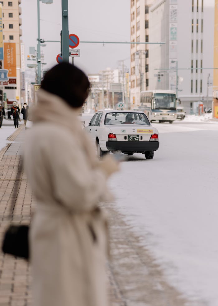 A blurred woman in winter attire stands on a snowy street in Sapporo as traffic passes by.