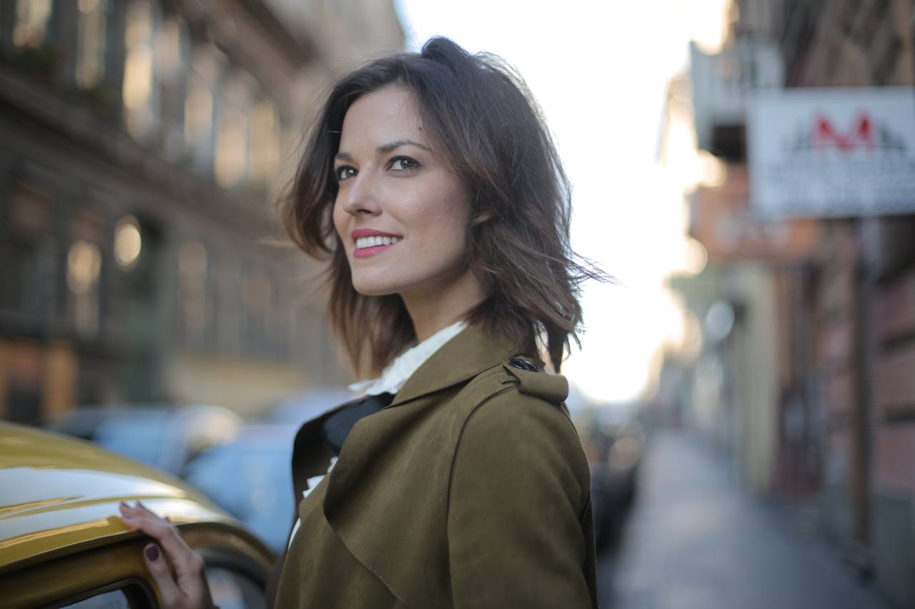 Portrait of a fashionable woman smiling beside a yellow taxi on a lively city street.